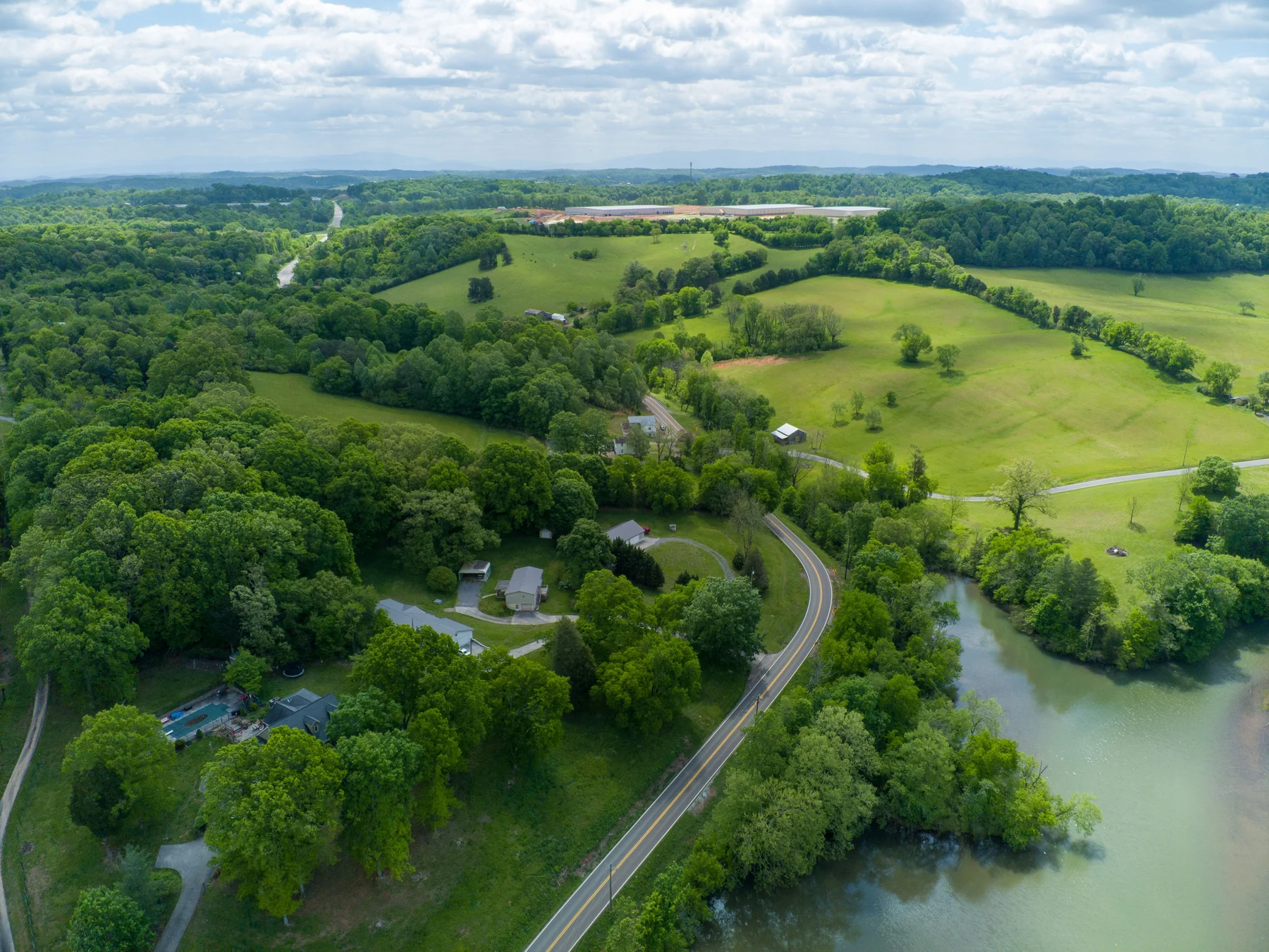 A curving road beside water, fields and trees, photographed from above