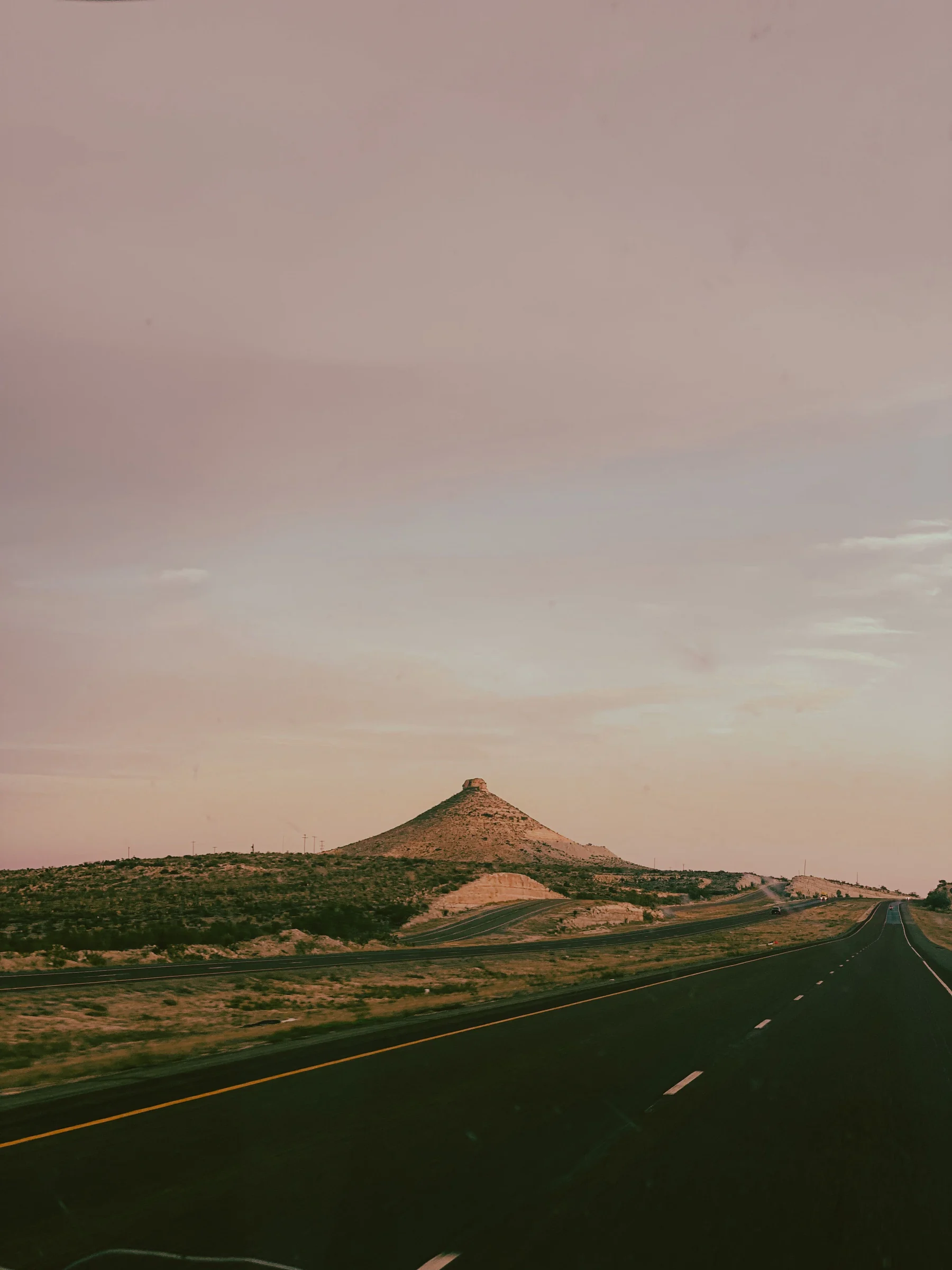 A paved road beside a low rocky hill beneath a broad sky